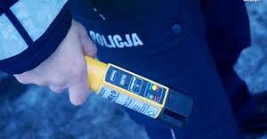 Policjant trzymający w ręku żółte urządzenie do badania stanu trzeźwości.