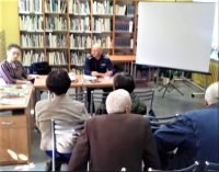 Dzielnicowy oraz Powiatowy Rzecznik Konsumenta znajdują się w bibliotece w Poddębicach. W spotkaniu uczestniczą okoliczni mieszkańcy. Osoby na zdjęciu siedzą i rozmawiają.