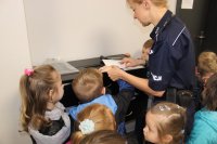 policjantka odbija linie papilarne palca dziecka, które zgłosiło się na ochotnika podczas wizyty w komendzie