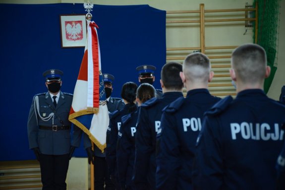 Na zdjęciu widać umundurowanych funkcjonariuszy policji w tle sztandar policji i  godło RP.