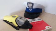 Na zdjęciu czapka policyjna, kodeks drogowy i urządzenie do pomiaru alkoholu w wydychanym powietrzu.