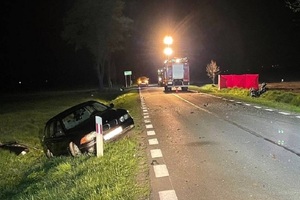 miejsce wypadku drogowego, po prawej widoczne bmw stojące w rowie, po lewej rozbity motocykl lezący na poboczu. W tle wóz strażacki oraz czerwony parawan do oględzin