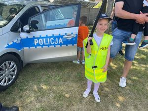 dzieci z policjantami ubrani w kamizelkę odblaskową na tle radiowozu