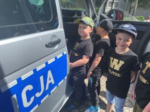 dzieci z policjantami ubrani w kamizelkę odblaskową na tle radiowozu