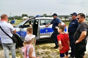 Policjanci przy radiowozie, osoby oglądają radiowóz.