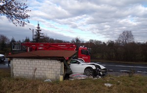 Zdjęcia z miejsca zdarzenia, rozbite białe auto, w tle wiata przystanku.