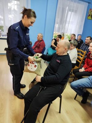 Spotkanie z pensjonariuszami. Policjantki stoją przed zgromadzonymi seniorami.