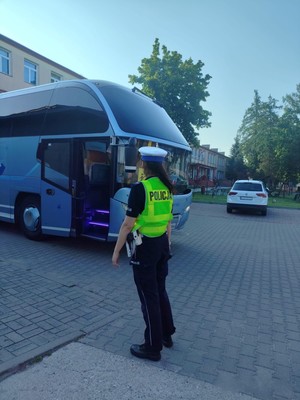 Policjantka stojąca przed autokarem, sprawdzająca stan ogumienia.