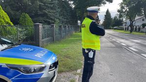 Policjant mierzący prędkość, z lewej strony radiowóz.