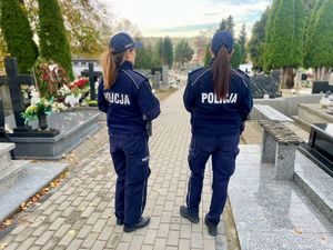 Policjanci przy radiowozie, w tle cmentarz.