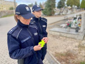 Policjanci przy radiowozie, w tle cmentarz.