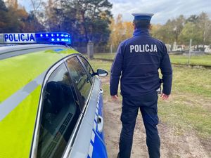 Policjanci przy radiowozie, w tle cmentarz.