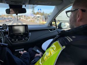 Policjanci przy radiowozie, w tle cmentarz.