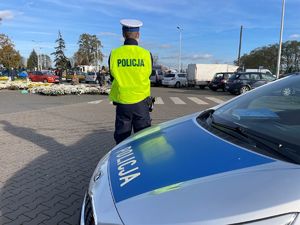 Policjanci przy radiowozie, w tle cmentarz.