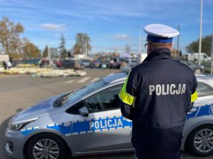 Policjanci przy radiowozie, w tle cmentarz.