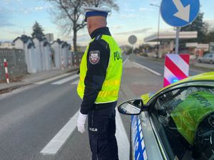 Policjanci przy radiowozie, w tle cmentarz.