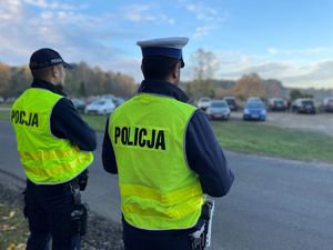 Policjanci przy radiowozie, w tle cmentarz.