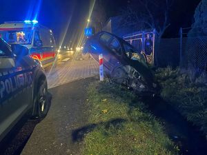 Z lewej strony radiowóz, z prawej strony uszkodzony pojazd leżący w rowie, w tle karetka pogotowia.