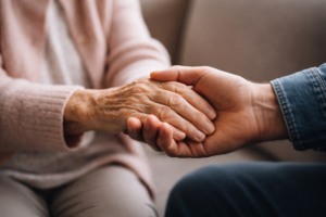 Dłoń seniorki trzymana przez dłoń mężczyzny.