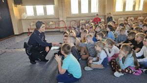 Policjantka rozmawia z dziećmi trzymając mikrofon.