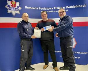 Policjanci i stojący wśród nich mężczyzna odbierający prezenty.