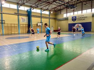 Zawodnicy grający w piłkę na hali sportowej.