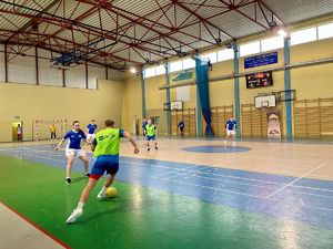 Zawodnicy grający w piłkę na hali sportowej.