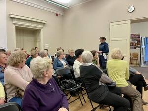 Seniorzy na debacie społecznej, w tle prelegenci.