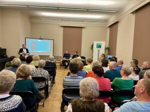 Seniorzy na debacie społecznej, w tle prelegenci.