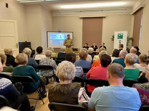 Seniorzy na debacie społecznej, w tle prelegenci.