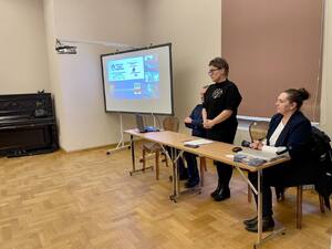 Seniorzy na debacie społecznej, w tle prelegenci.