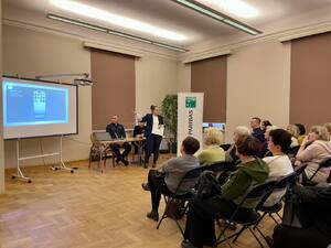 Seniorzy na debacie społecznej, w tle prelegenci.