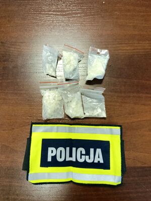 Sześć woreczków foliowych z białą substancją, pod nimi opaska z napisem Policja.