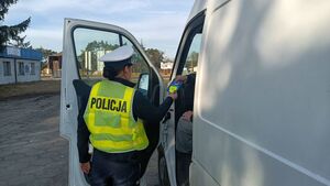 Funkcjonariuszka wręcza odblask i ulotkę kierującemu siedzącemu w aucie.