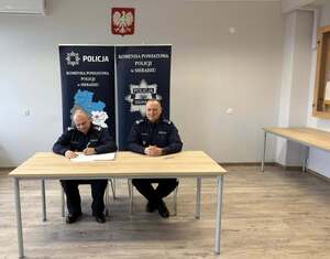 Panowie Komendanci za biurkiem podpisują dokument.