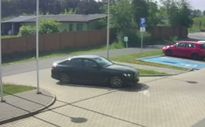 Zdjęcie z zapisu monitoringu - wjeżdżające czarne auto na parking komendy.