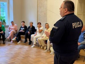 Policjant a wokół seniorzy zgromadzeni na sali.