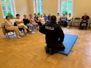 Policjant a wokół seniorzy zgromadzeni na sali.