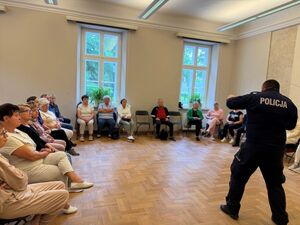 Policjant a wokół seniorzy zgromadzeni na sali.