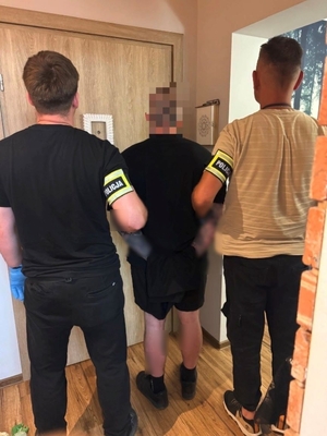 Dwóch nieumundurowanych policjantów stoi z zatrzymanym mężczyzną.
