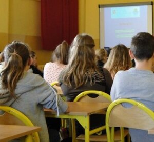 Uczniowie gimnazjum siedzą w ławkach, znajdują się w klasie i oglądają spot "Szkoda Ciebie na takie patoklimaty"