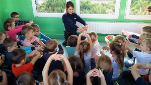 Policjantka prezentuje bezpieczną pozycję przed atakiem psa, dzieci ją naśladują.